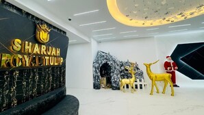 A modern interior with a black wall featuring 'SHARJAH ROYAL TULIP' text, a white ceiling with a circular light fixture, and a white wall with a Santa Claus figure and a deer statue. - Palette Sharjah Aparthotel formerly Royal Tulip (Sharjah)