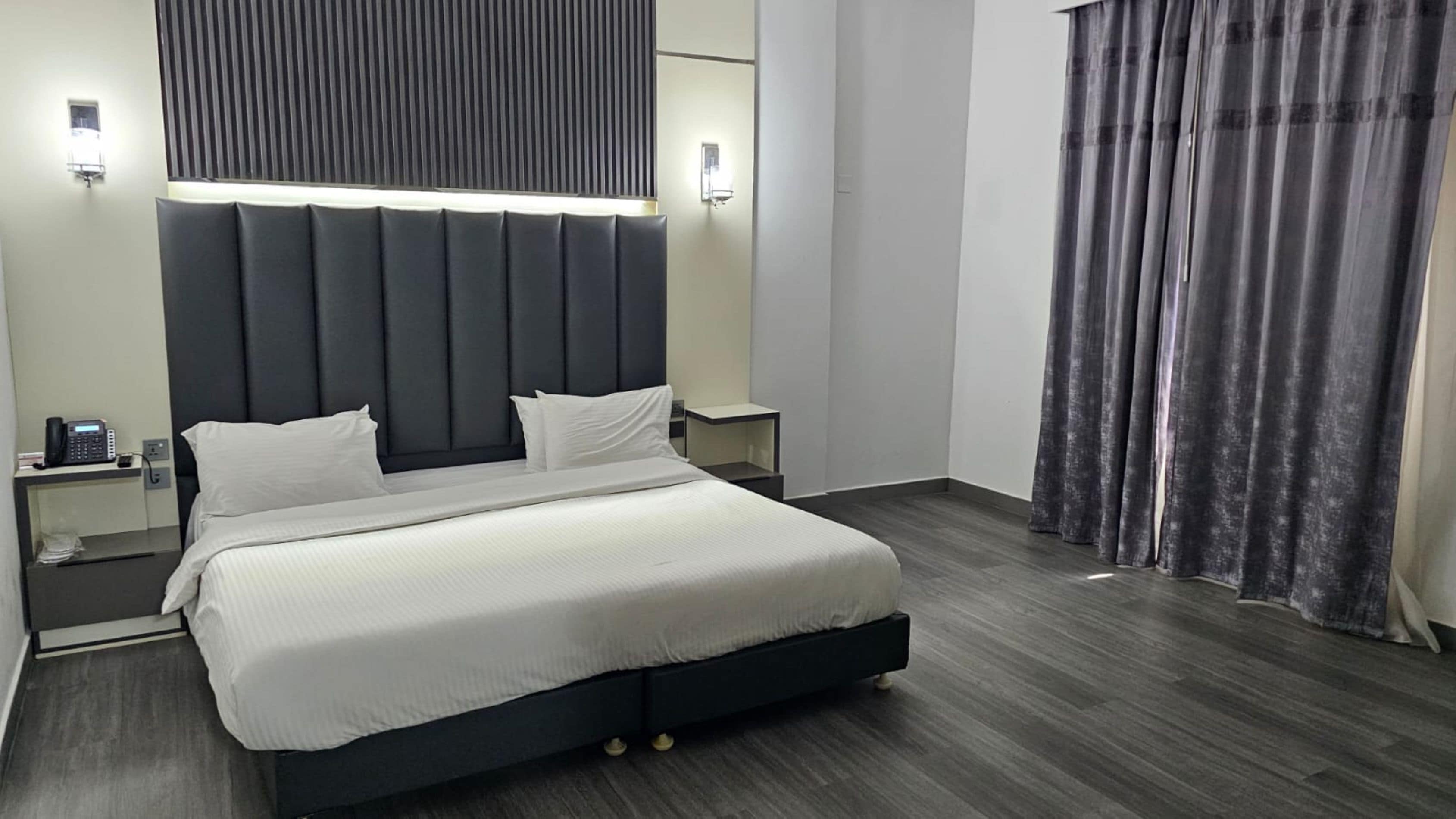 Una habitación de hotel moderna con una cama grande, mesitas de noche, un teléfono y una cortina.