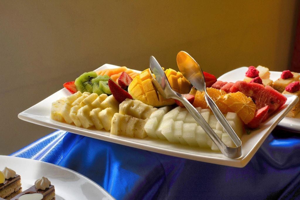 A fruit platter with various fruits and a spoon on a white plate.