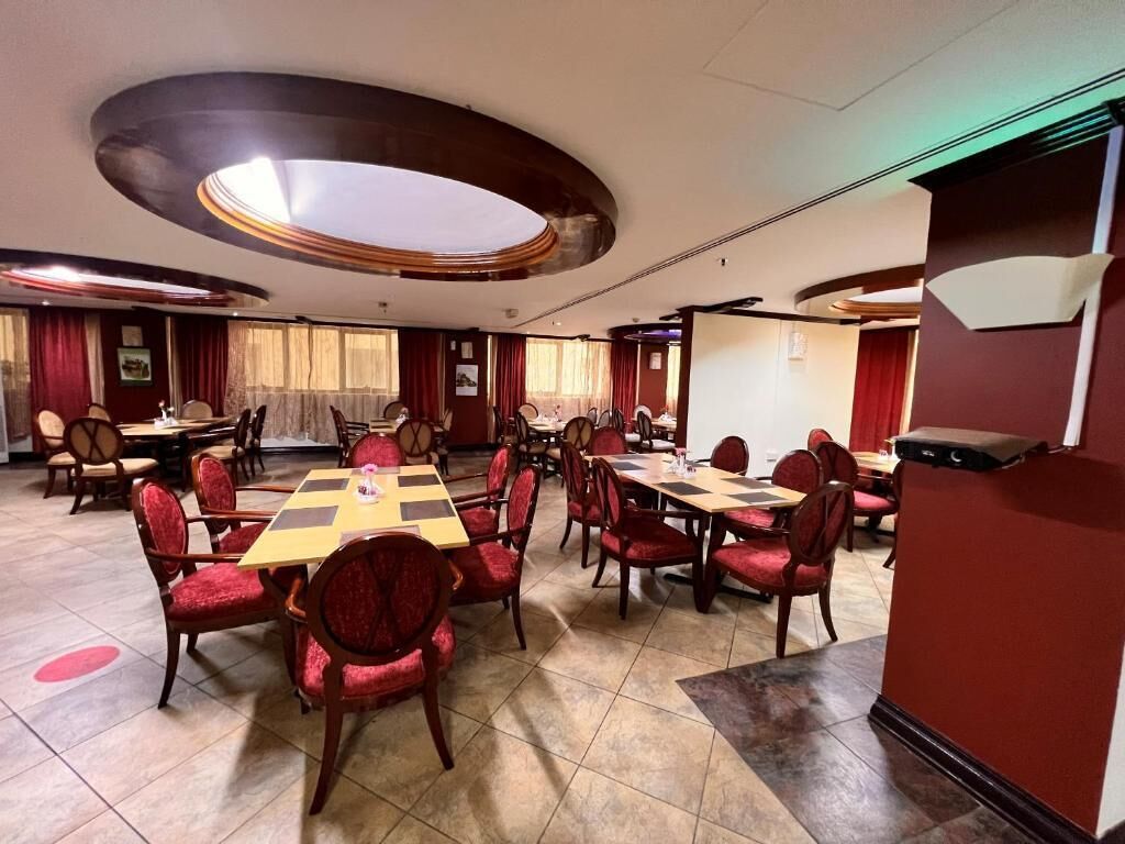 Un salón de conferencias con varias mesas y sillas, un escenario y una pared de acento roja.