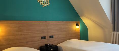 A hotel room with two beds, a wooden headboard, a wall-mounted light, and a small table with a phone.