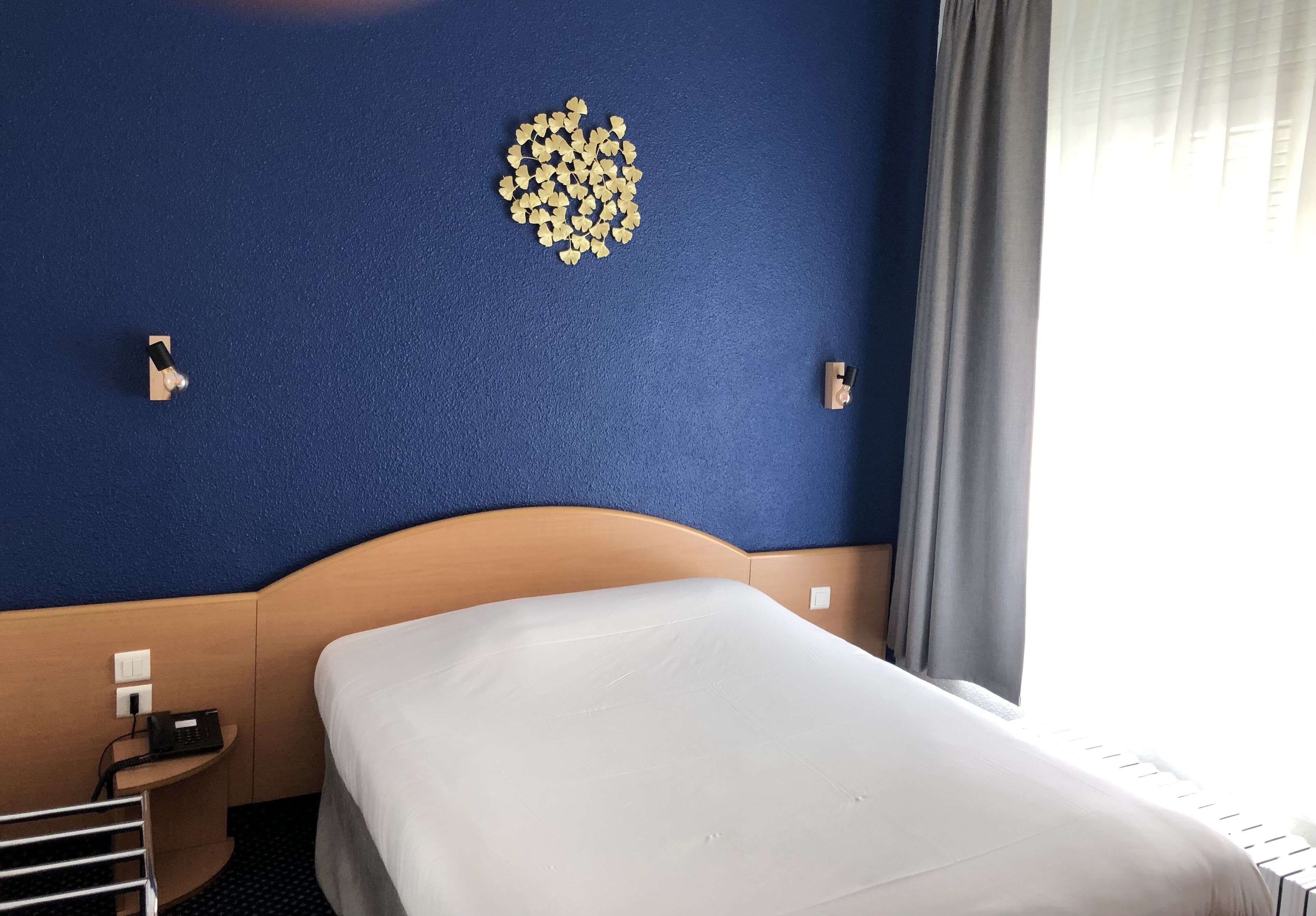 Una habitación de hotel con una cama bien hecha, una mesita de noche pequeña con un teléfono y una decoración en la pared.