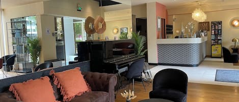 A modern lobby with a brown sofa, a round marble table, a piano, and a reception desk.