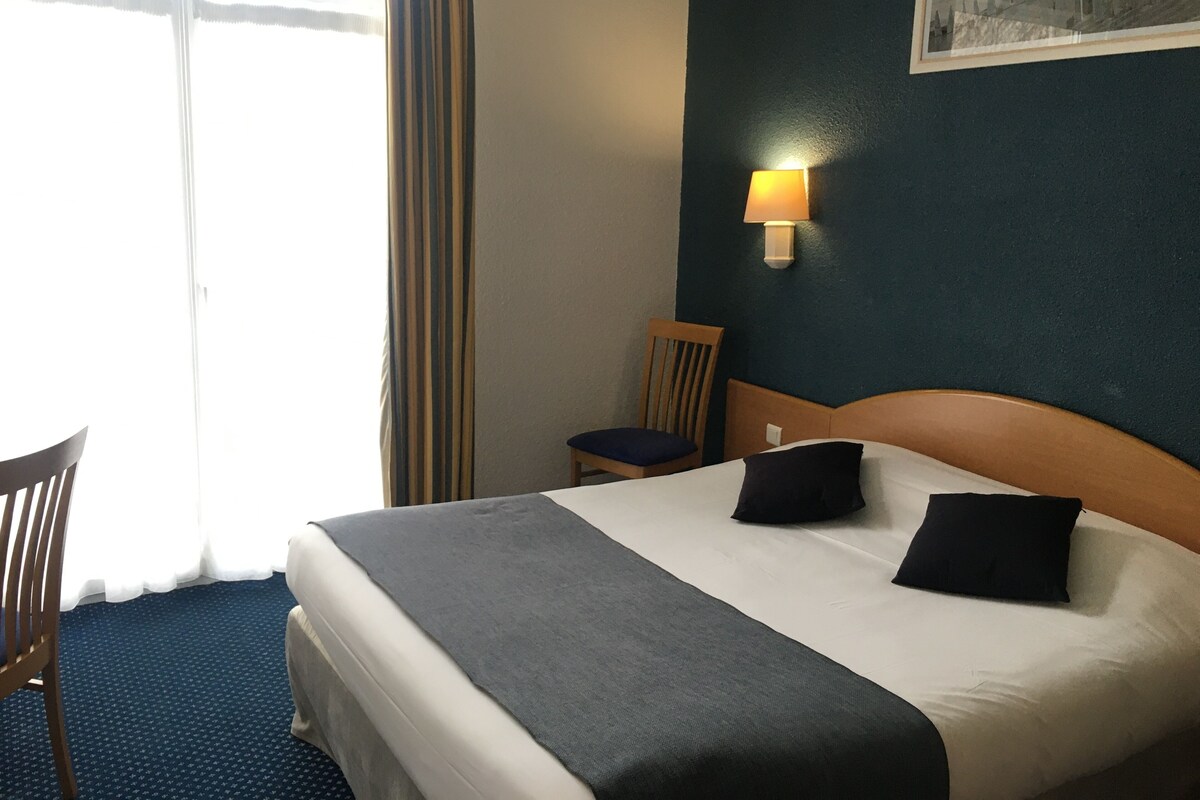 Quarto de hotel com cama, cadeira, abajur e um quadro na parede.