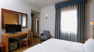 A hotel room with a bed, a desk with a television, a chair, a small table, and a mirror.