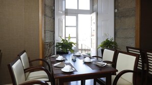 A dining area with a wooden table set for four, surrounded by chairs, with potted plants and a view of the outdoors. - Montebelo Palácio dos Melos Viseu Historic Hotel (Viseu)