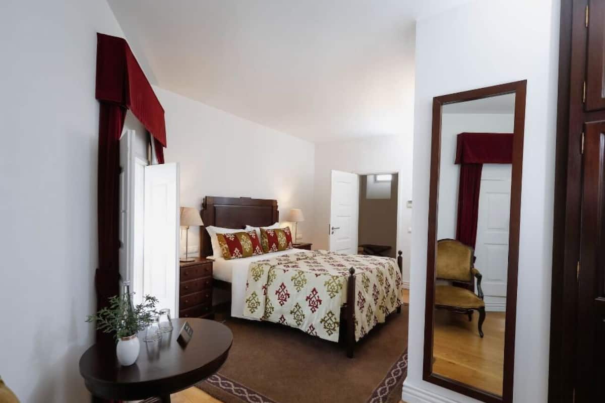 A bedroom with a bed, bedside tables, a mirror, a chair, and a small table with a plant.