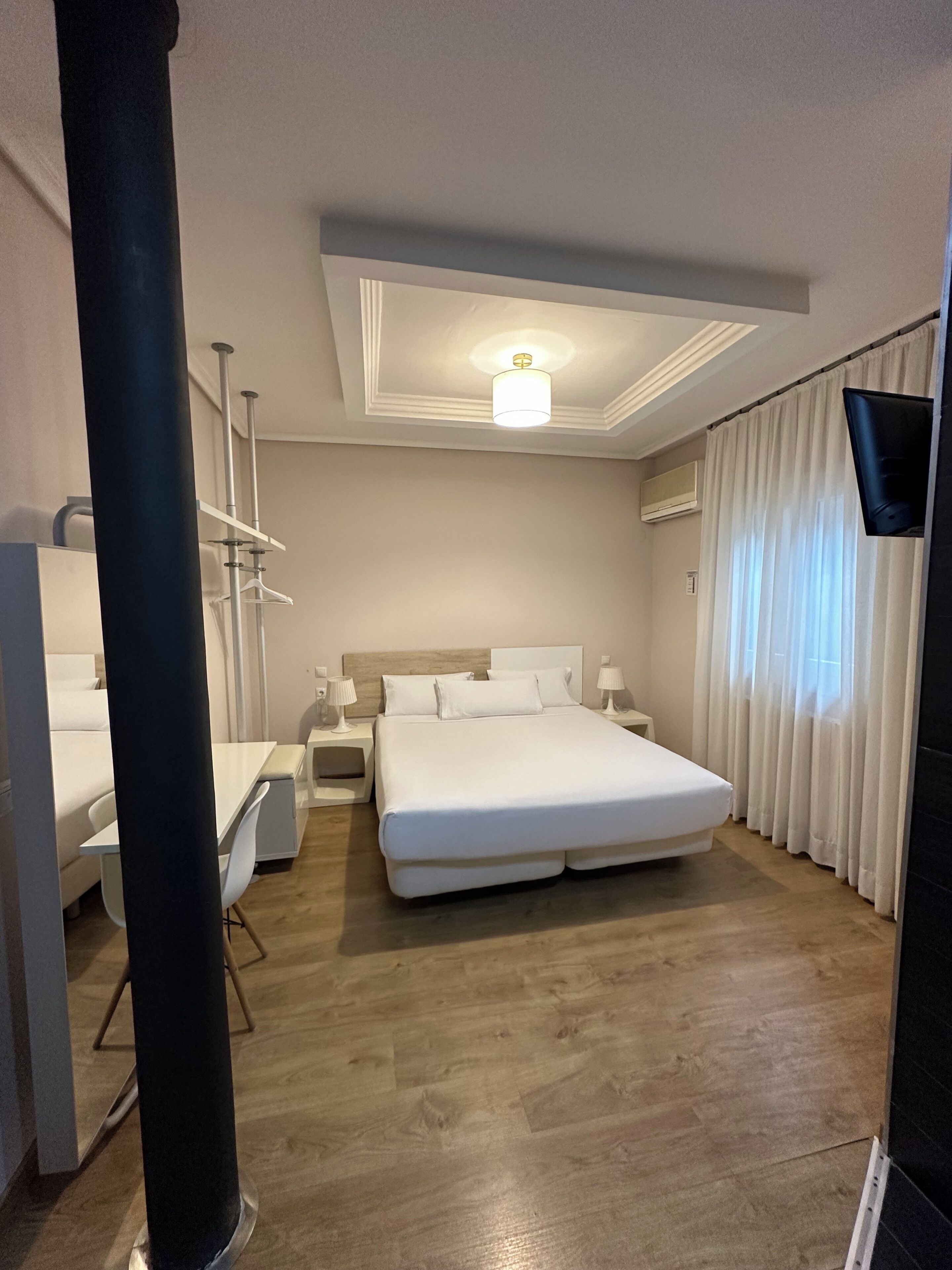Et moderne hotelværelse med en stor seng, sengeborde, et skrivebord og et fladskærms-tv.