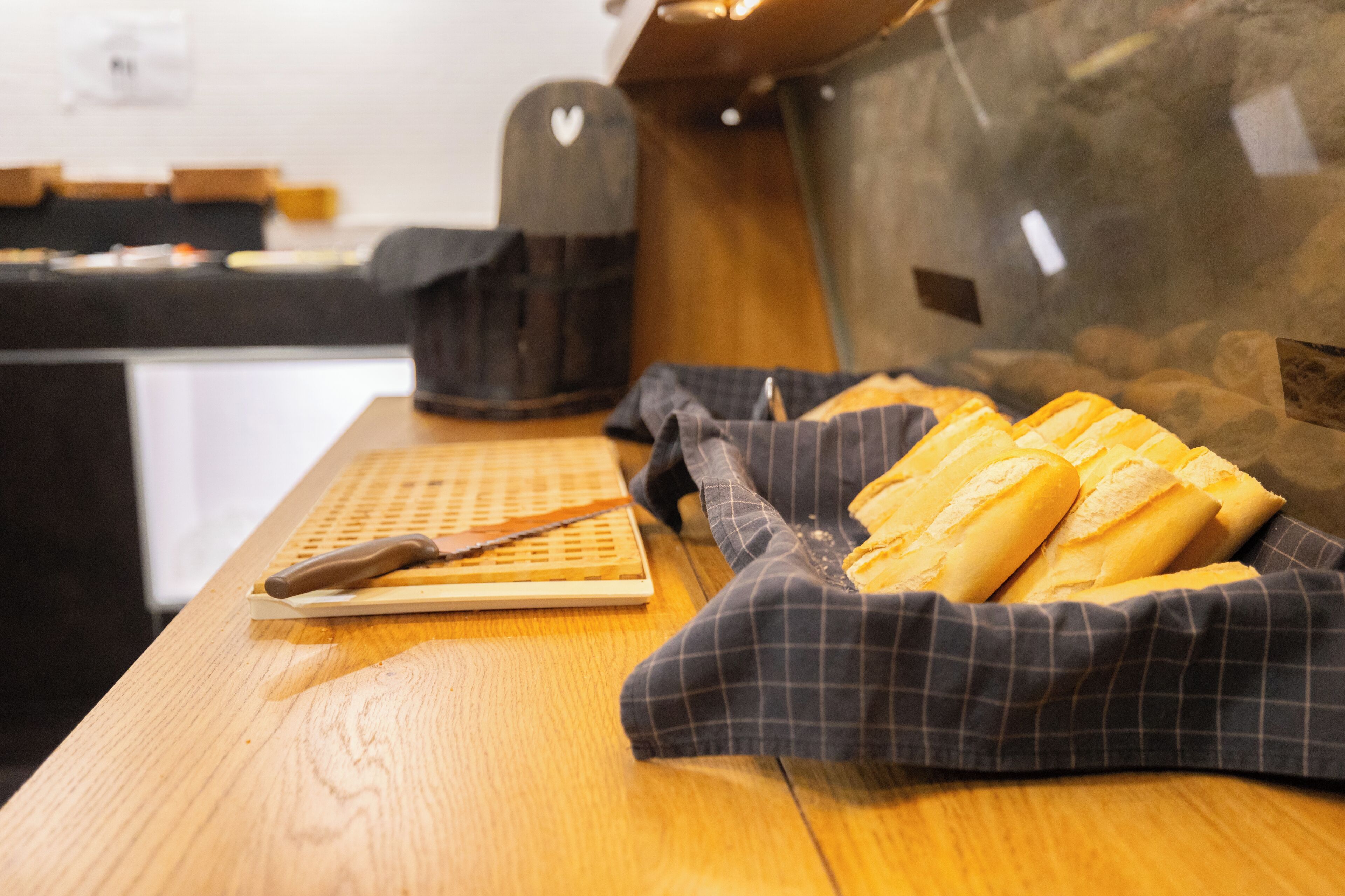 Una encimera de cocina con baguettes en una cesta, una tabla de cortar y un cuchillo.