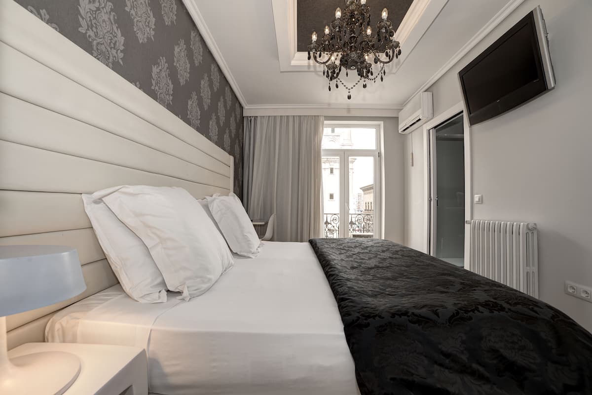 A modern bedroom with a large bed, a bedside table, a chandelier, a television, and a view of the outside.