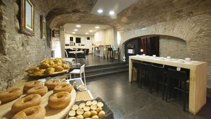 Un restaurante con paredes de piedra, una larga mesa de madera y una variedad de productos horneados a la vista.
