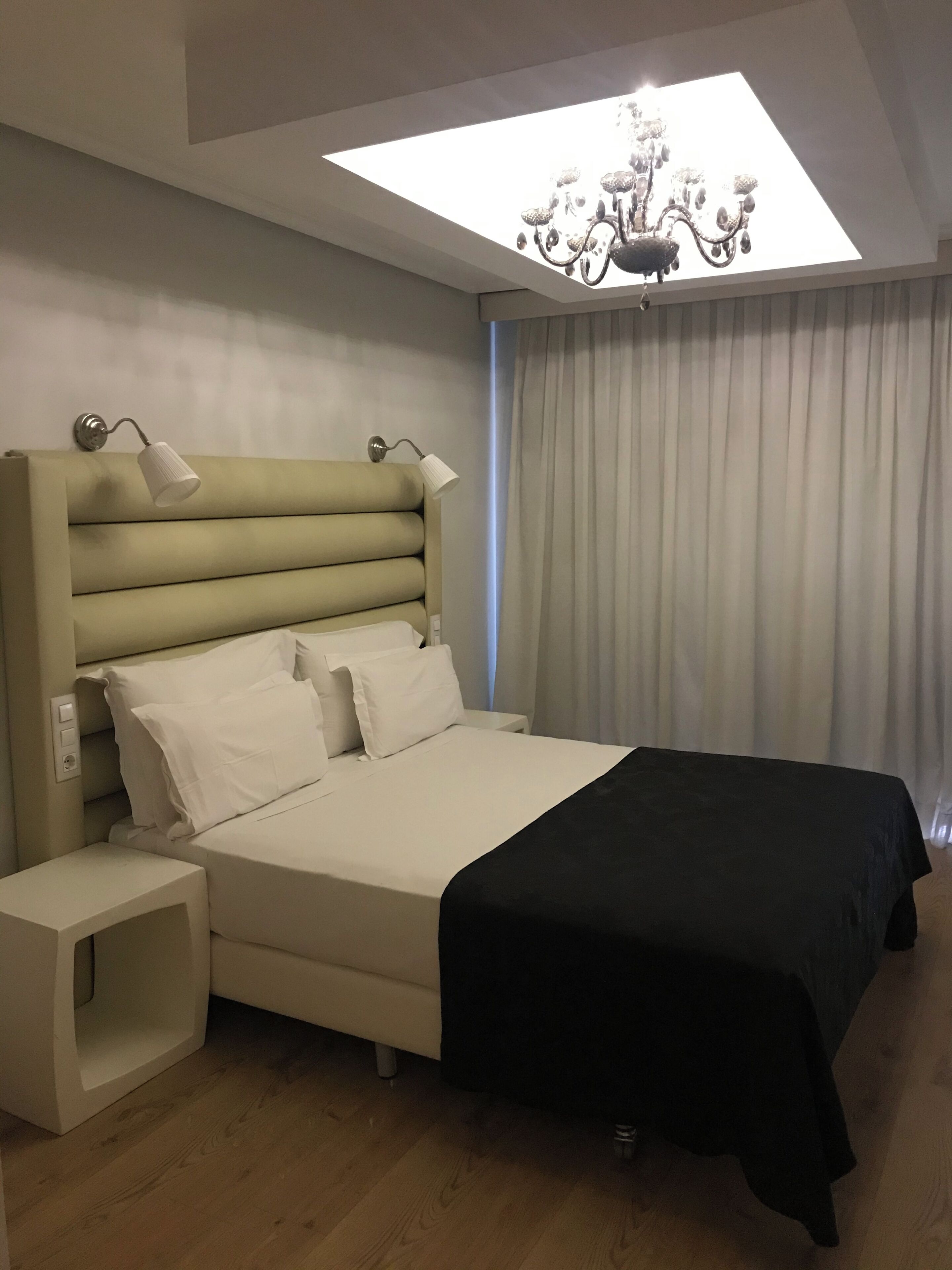 Un dormitorio moderno con cama, mesitas de noche, una araña y un tragaluz.