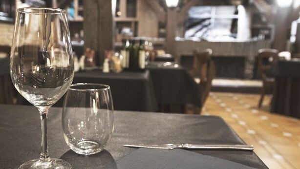Una mesa de comedor con una copa de vino, un vaso más pequeño y cubiertos sobre un mantel individual negro.