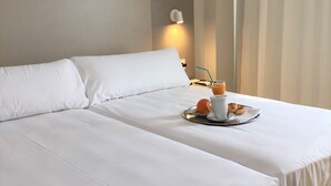 Habitación de hotel con una cama bien hecha, una bandeja con desayuno que incluye jugo de naranja, un croissant y una taza de café.