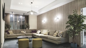 Una sala de estar moderna con un sofá modular, dos otomanas, una mesa de centro y una planta grande en maceta.