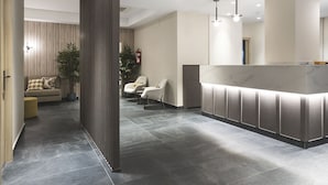 Una moderna zona de recepción con mostrador de mármol, área de estar con sofás y sillones, y una planta en maceta.