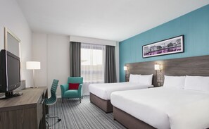 A hotel room with two beds, a desk with a TV, a chair, and a window with curtains.