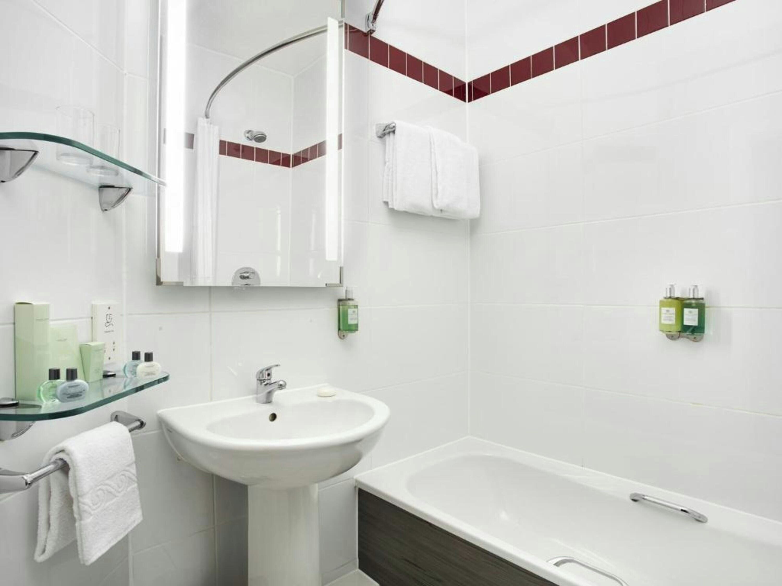 A bathroom with a glass shower enclosure, a pedestal sink, a bathtub, and a mirror.