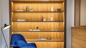 A modern room with a wooden bookshelf, a blue armchair, and a small table. - Leonardo Hotel Liverpool (Liverpool)