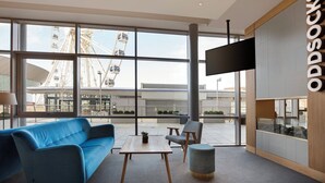 A modern interior with a large window, a blue sofa, a wooden table, and a grey ottoman. - Leonardo Hotel Liverpool (Liverpool)