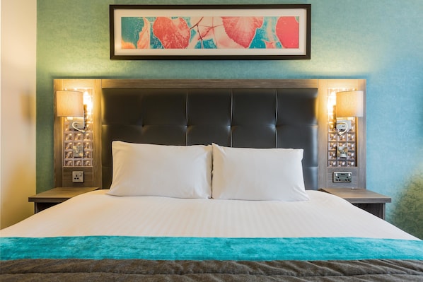 A neatly made bed with a teal throw blanket, a dark headboard, and two bedside lamps.
