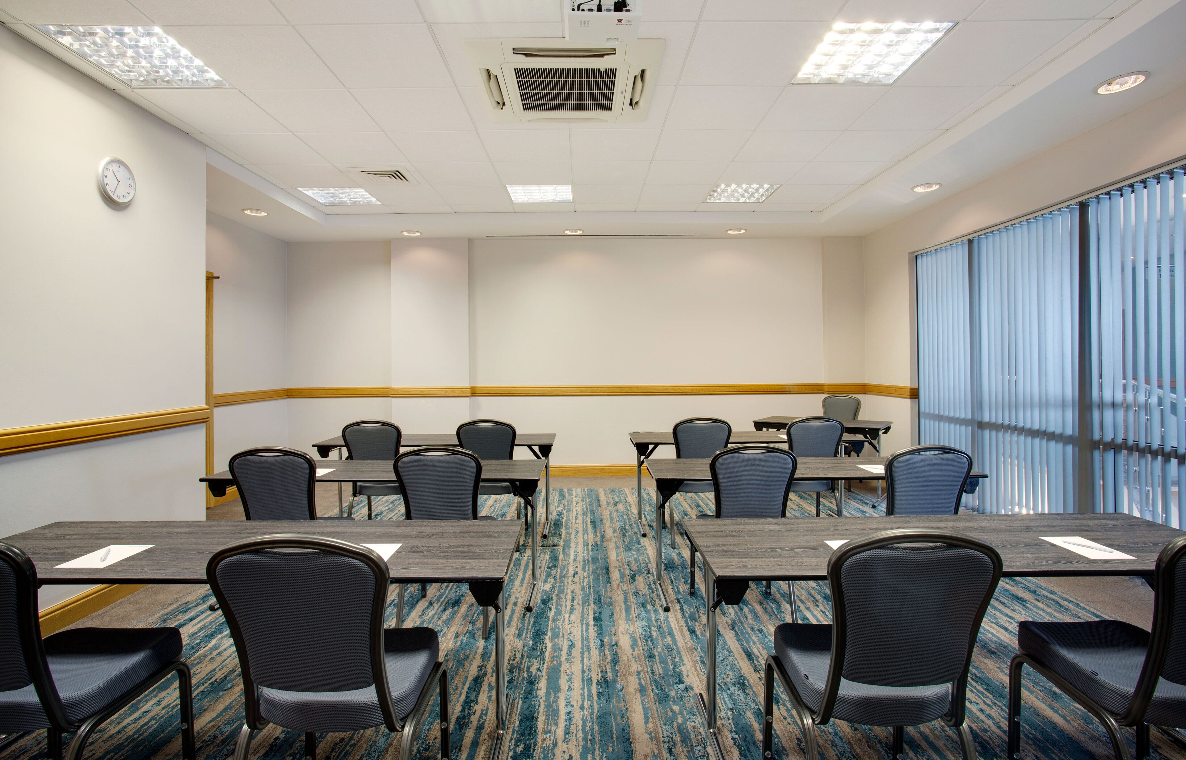 A conference room with a carpeted floor, tables, chairs, and a clock on the wall.