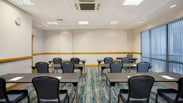 A conference room with a carpeted floor, tables, chairs, and a clock on the wall.