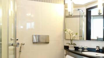 Un baño moderno con cabina de ducha de vidrio, lavamanos empotrado, espejo y una orquídea en maceta.