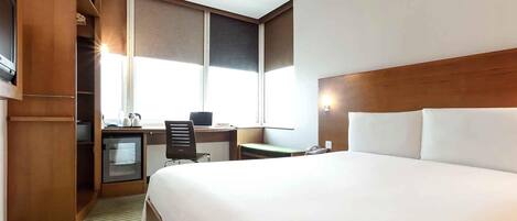 Habitación de hotel con una cama grande, un escritorio con silla, un televisor pequeño y una ventana.