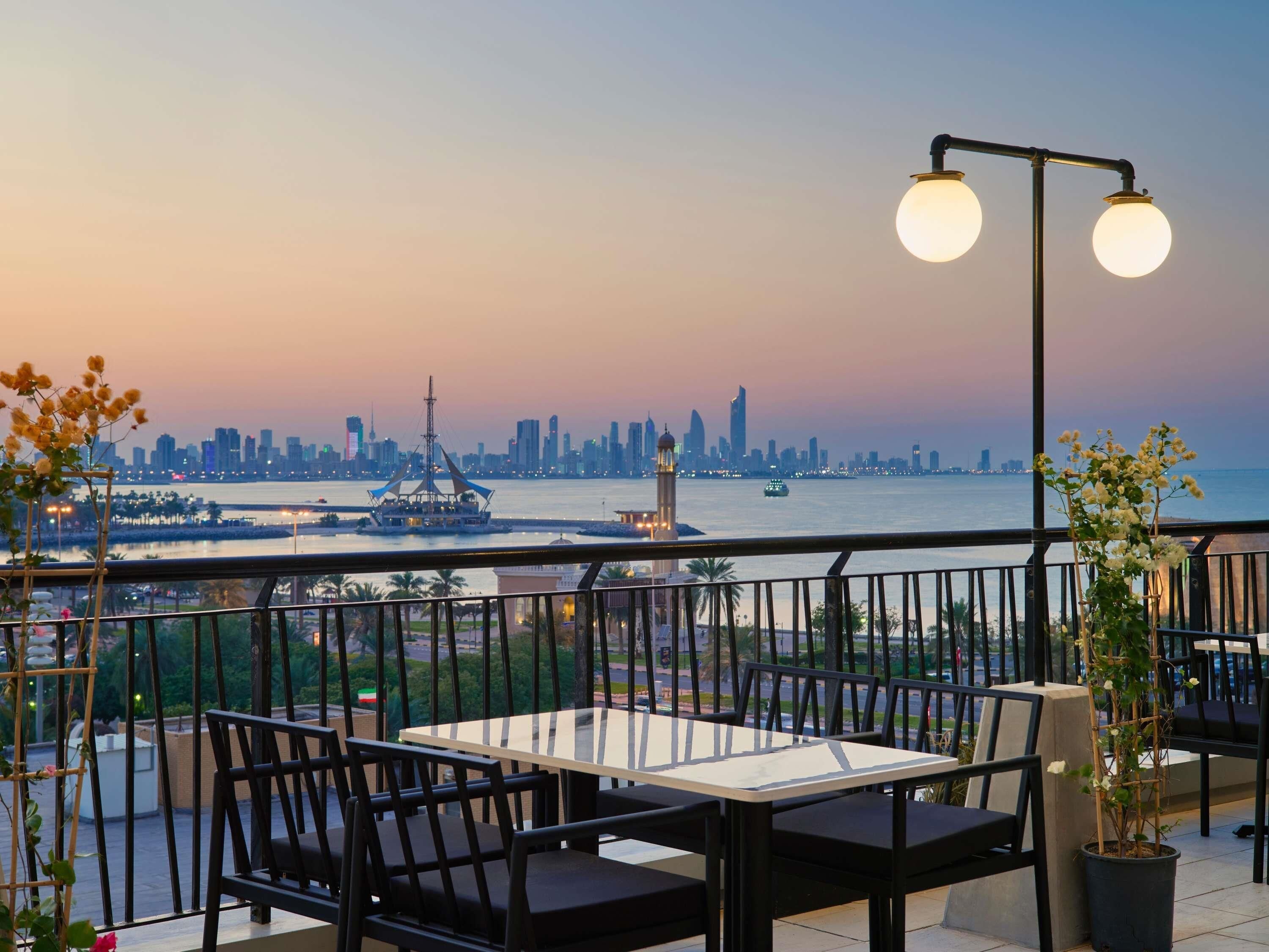 Eine Terrasse mit Tisch und Stühlen, mit Blick auf eine Stadtlandschaft und Wasser.
