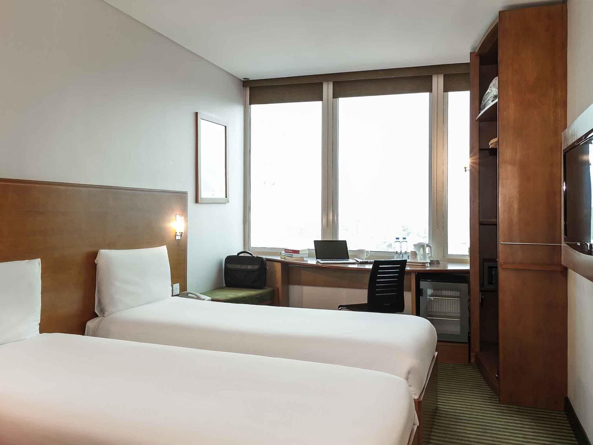 A hotel room with two beds, a desk with a laptop, a television, and a wardrobe.
