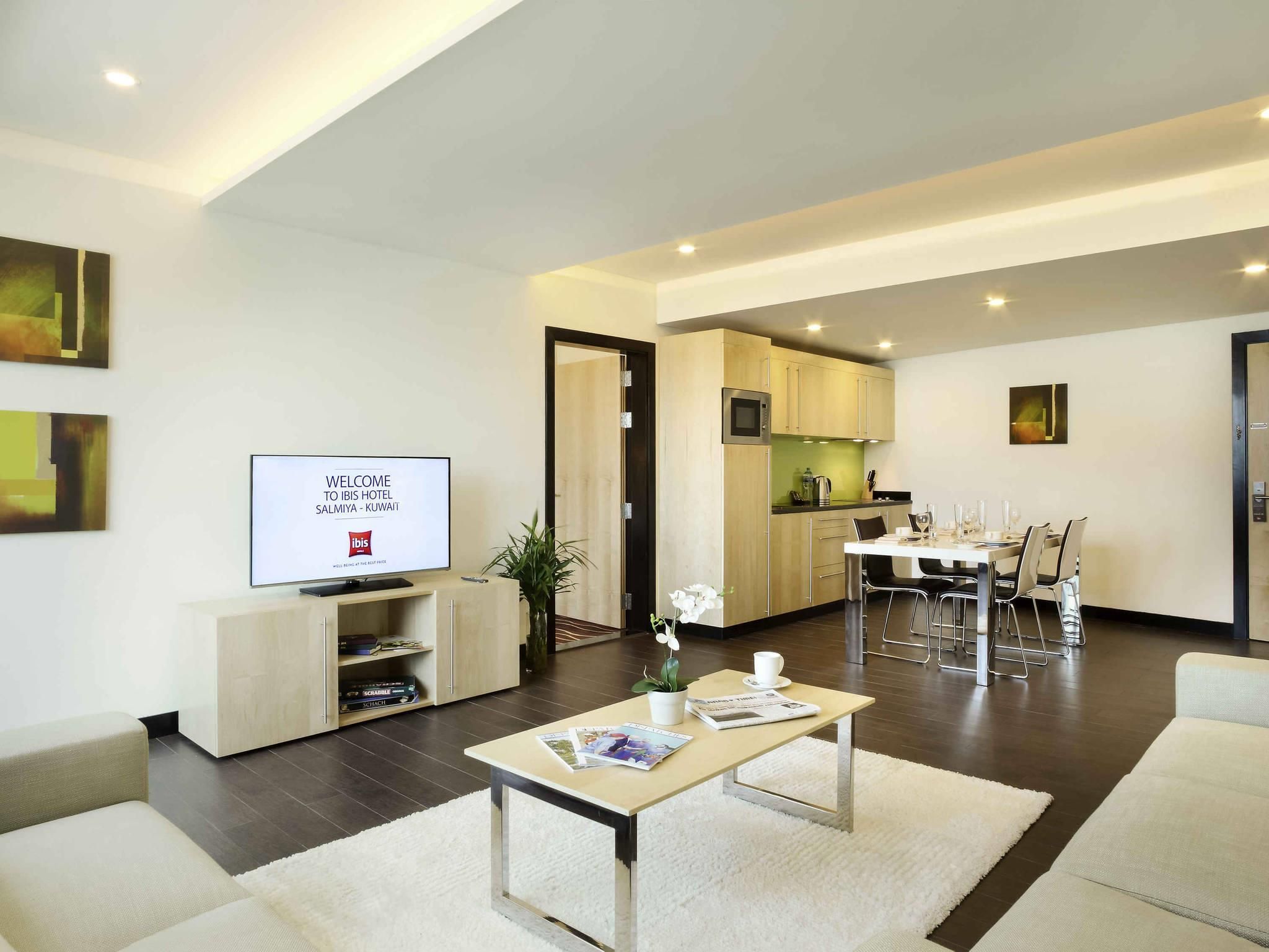 Una sala de estar moderna con un televisor de pantalla plana, una mesa de centro y un comedor, con una cocina visible al fondo.