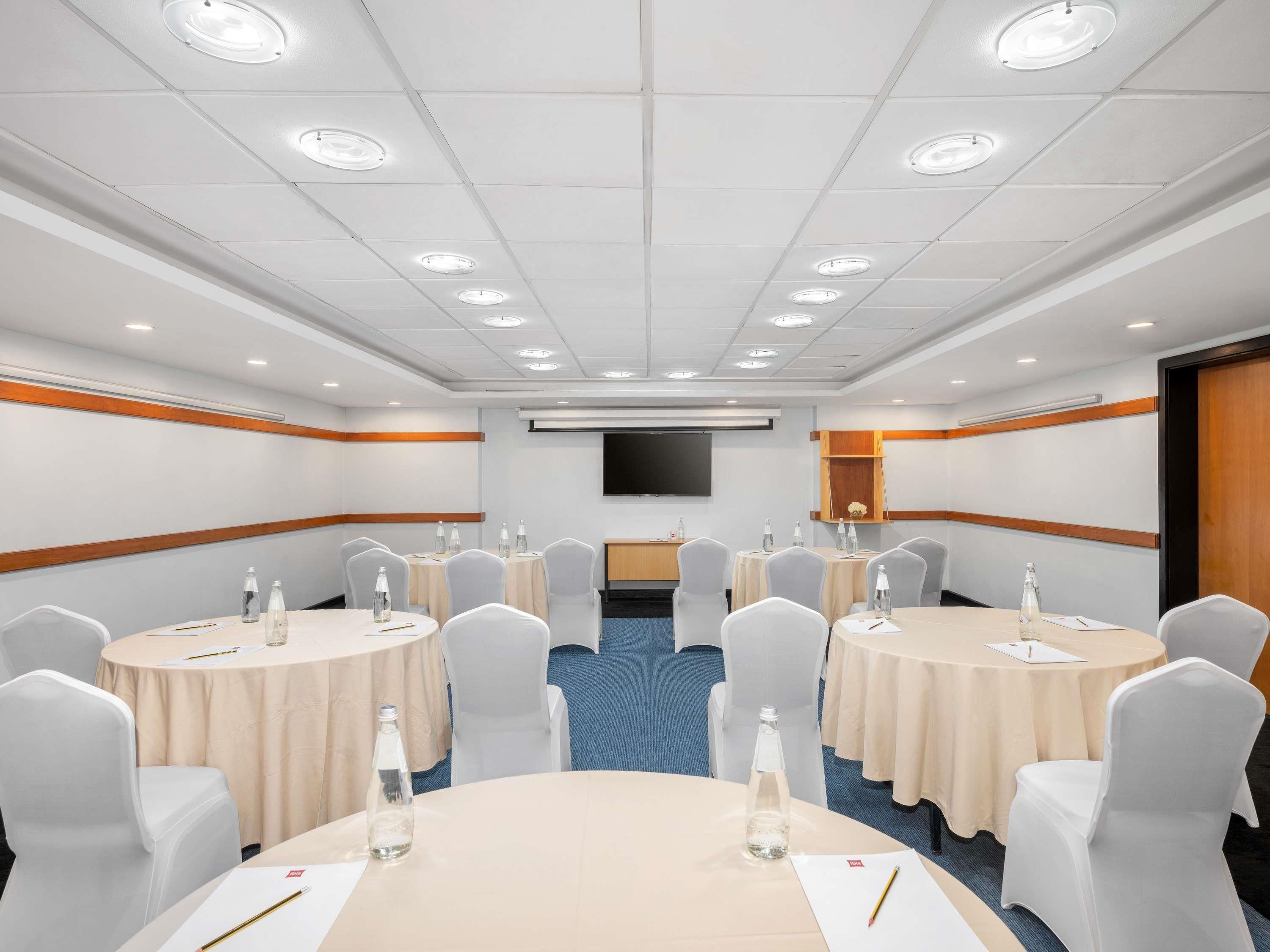 Un salón de conferencias con mesas redondas, sillas y un televisor de pantalla plana en la pared.