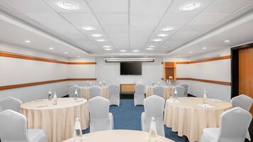 Un salón de conferencias con mesas redondas, sillas y un televisor de pantalla plana en la pared.