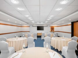 Un salón de conferencias con mesas redondas, sillas y un televisor de pantalla plana en la pared.
