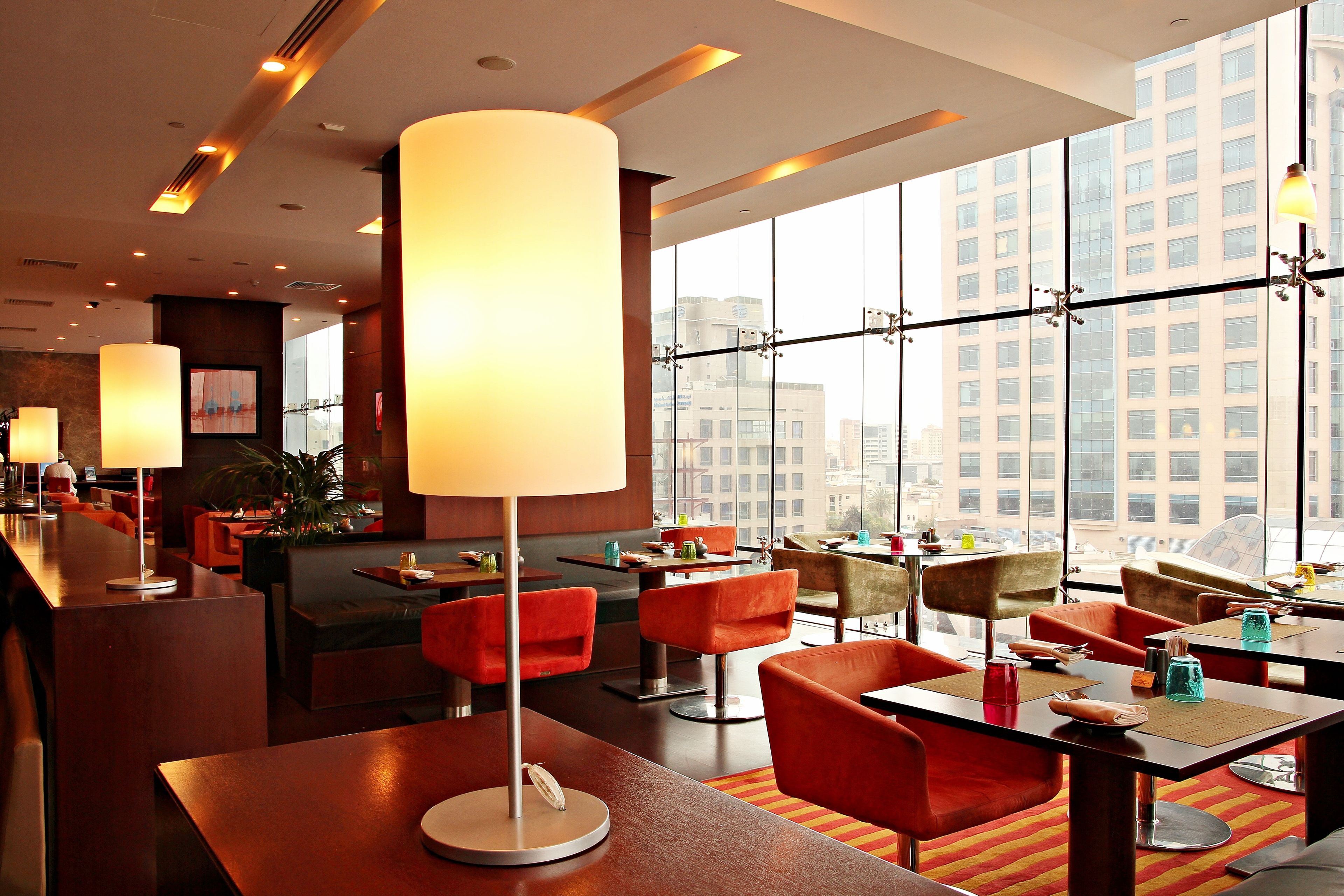 A modern hotel lobby with high ceilings, large windows, and a mix of seating areas including tables and chairs.