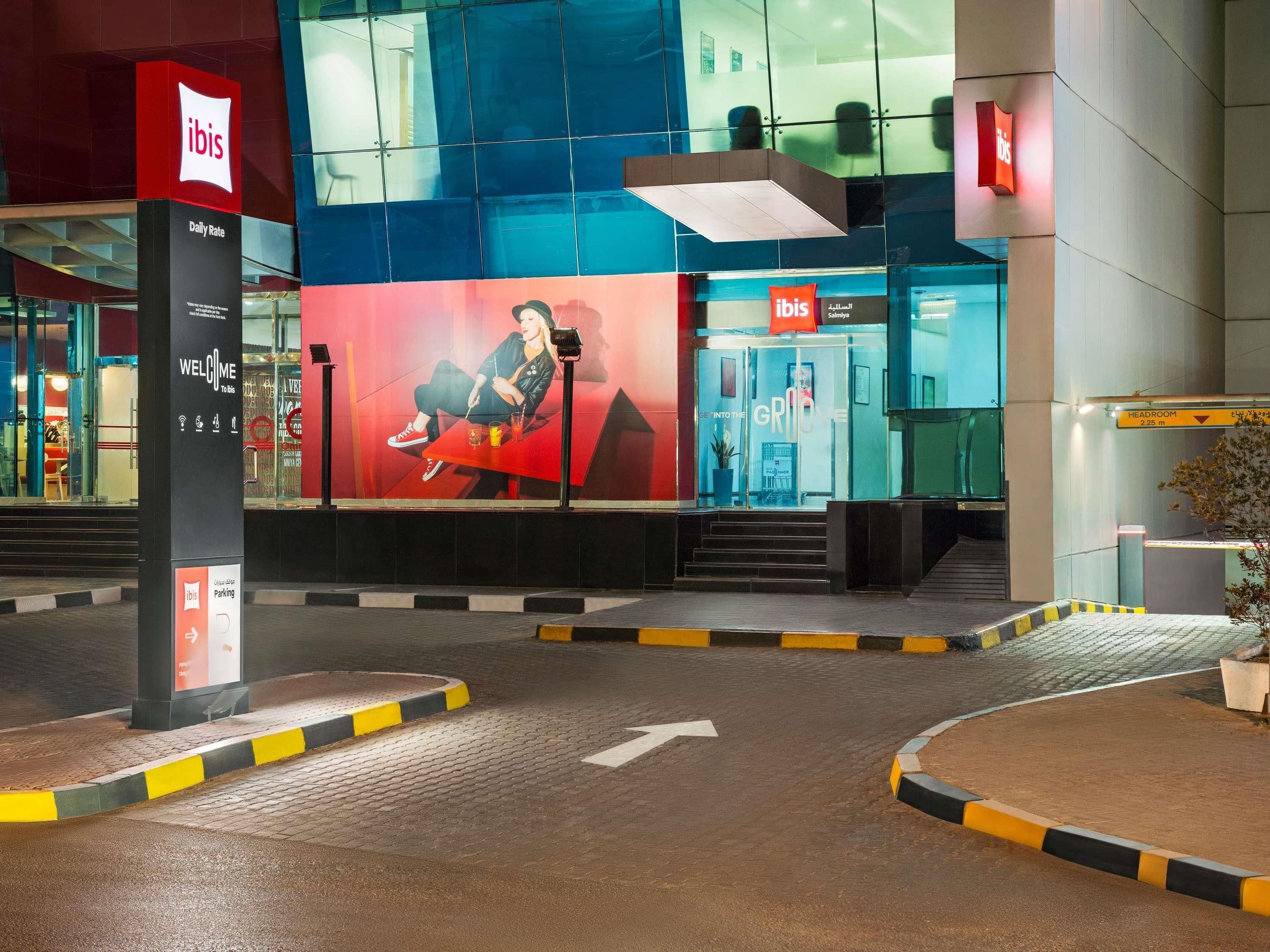 A modern building with an 'ibis' sign, a large outdoor advertisement, and a clear pathway leading to the entrance.