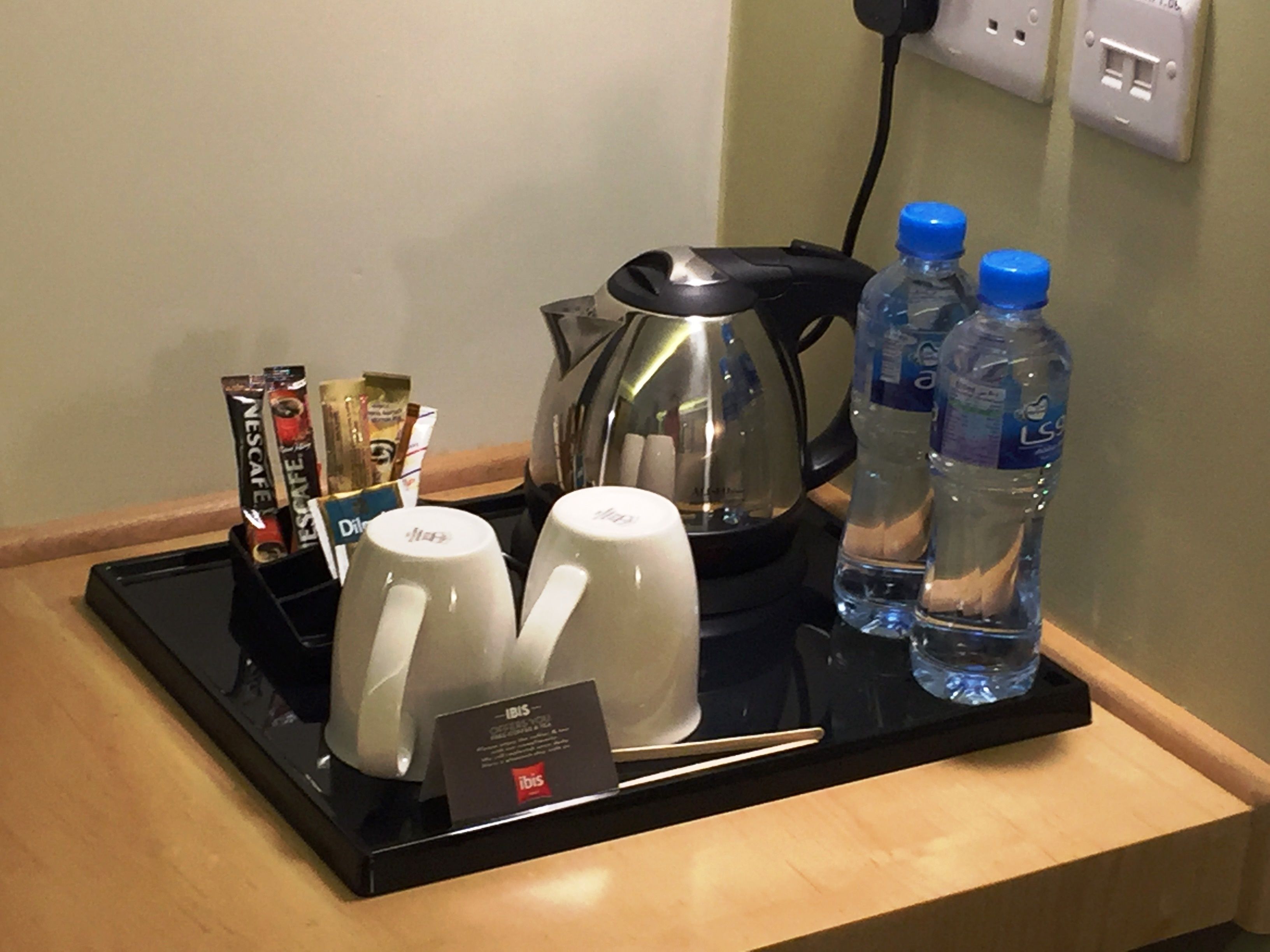 A tray with two white mugs, a coffee pot, a water bottle, and a card on a wooden surface.