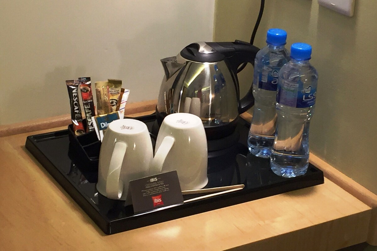 A tray with two white mugs, a coffee pot, a water bottle, and a card on a wooden surface.