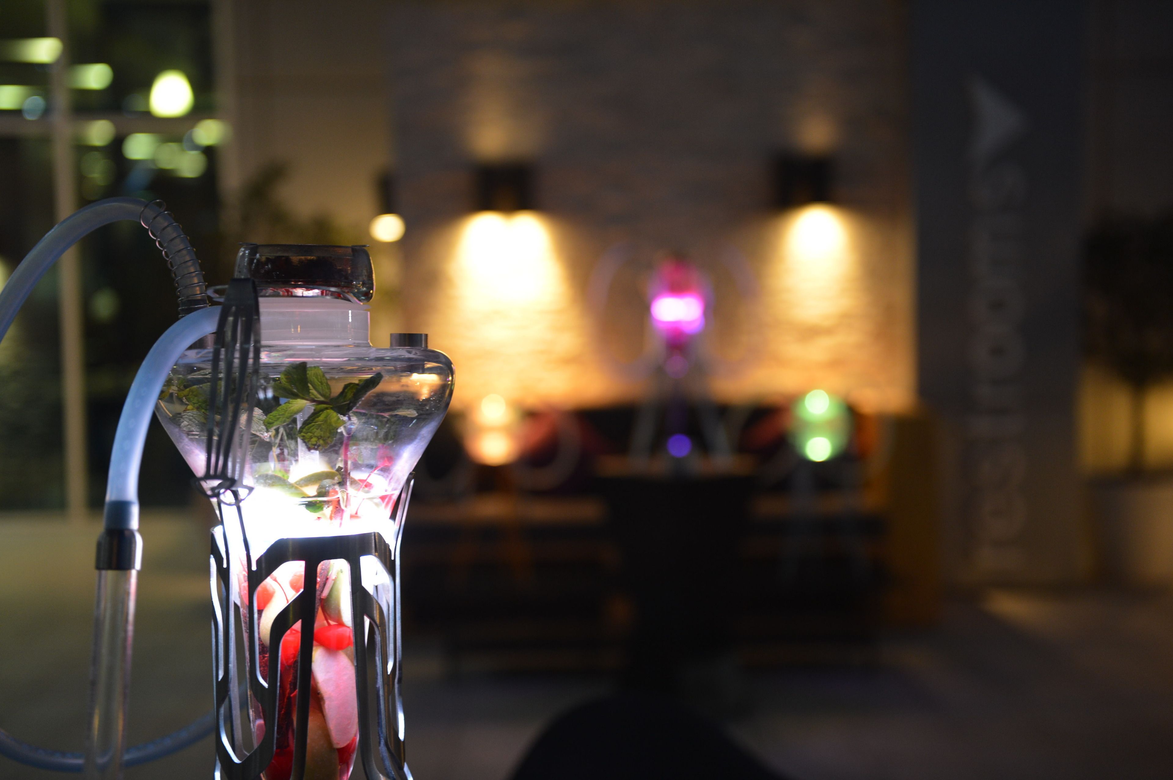 A hookah with a hose and a glass container filled with ice and a drink, set against a blurred background with warm lighting.