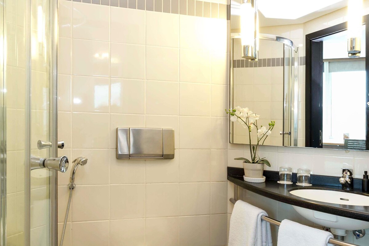 A modern bathroom with a glass shower enclosure, a built-in sink, a mirror, and a potted orchid.