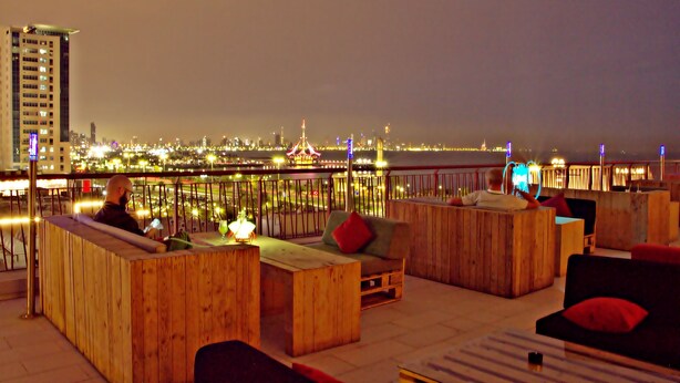 A rooftop bar with wooden furniture and a city view at night. - ibis Kuwait Salmiya (Salmiya)