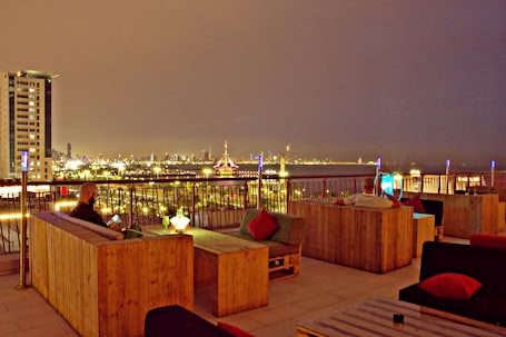 A rooftop bar with wooden furniture and a city view at night.