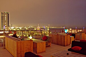 A rooftop bar with wooden furniture and a city view at night.