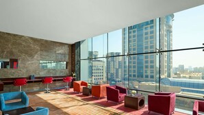 Un salón moderno con sillones rojos y azules, una alfombra estampada y vistas a la ciudad a través de amplias ventanas.