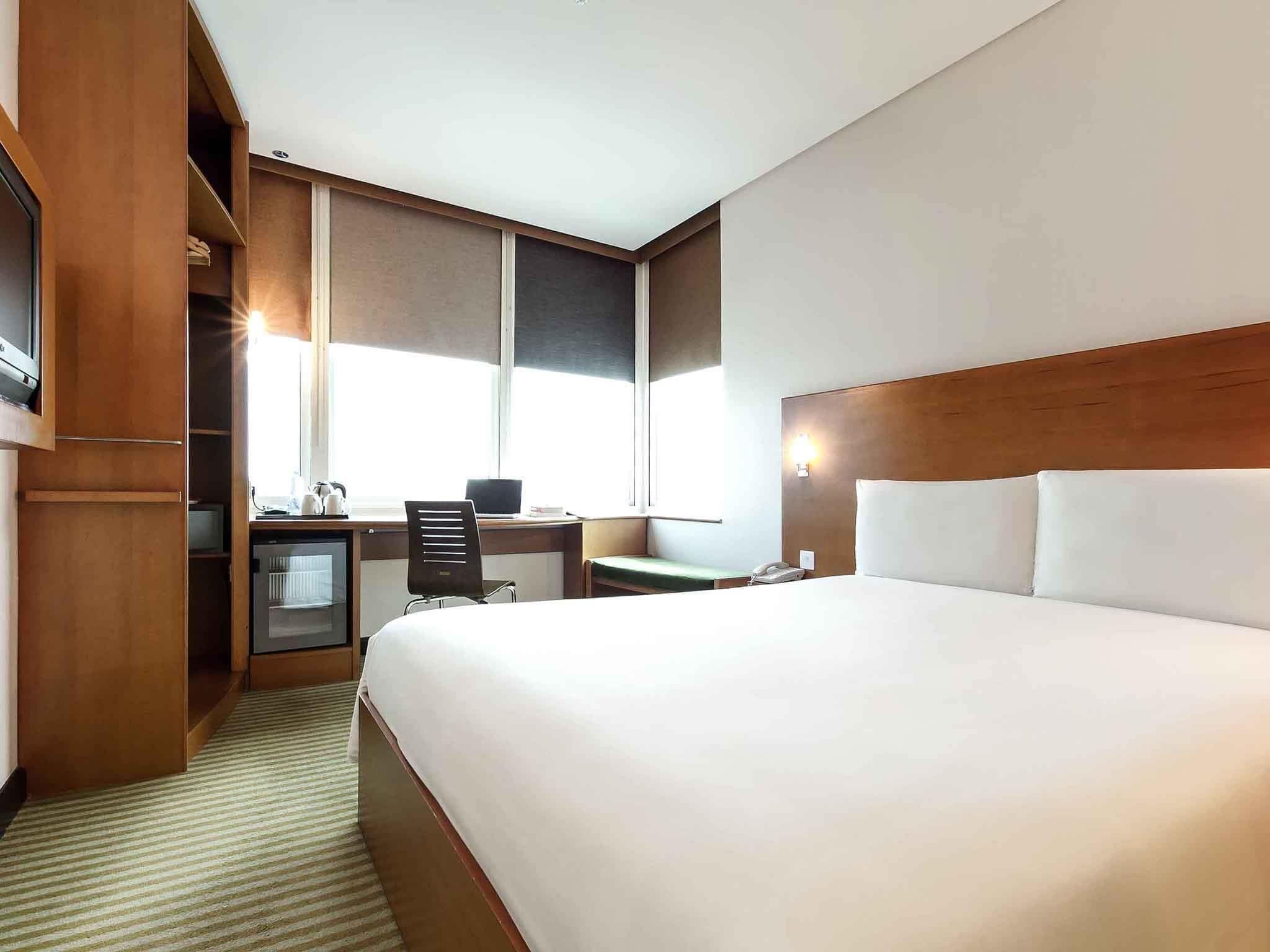 Habitación de hotel con una cama grande, un escritorio con silla, un televisor pequeño y una ventana.