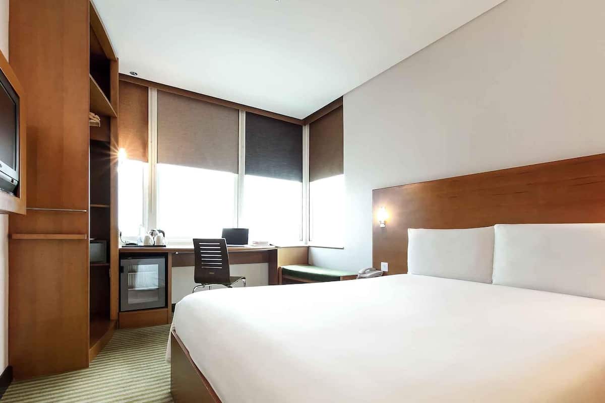 Ein Hotelzimmer mit einem großen Bett, einem Schreibtisch mit Stuhl, einem kleinen Fernseher und einem Fenster.
