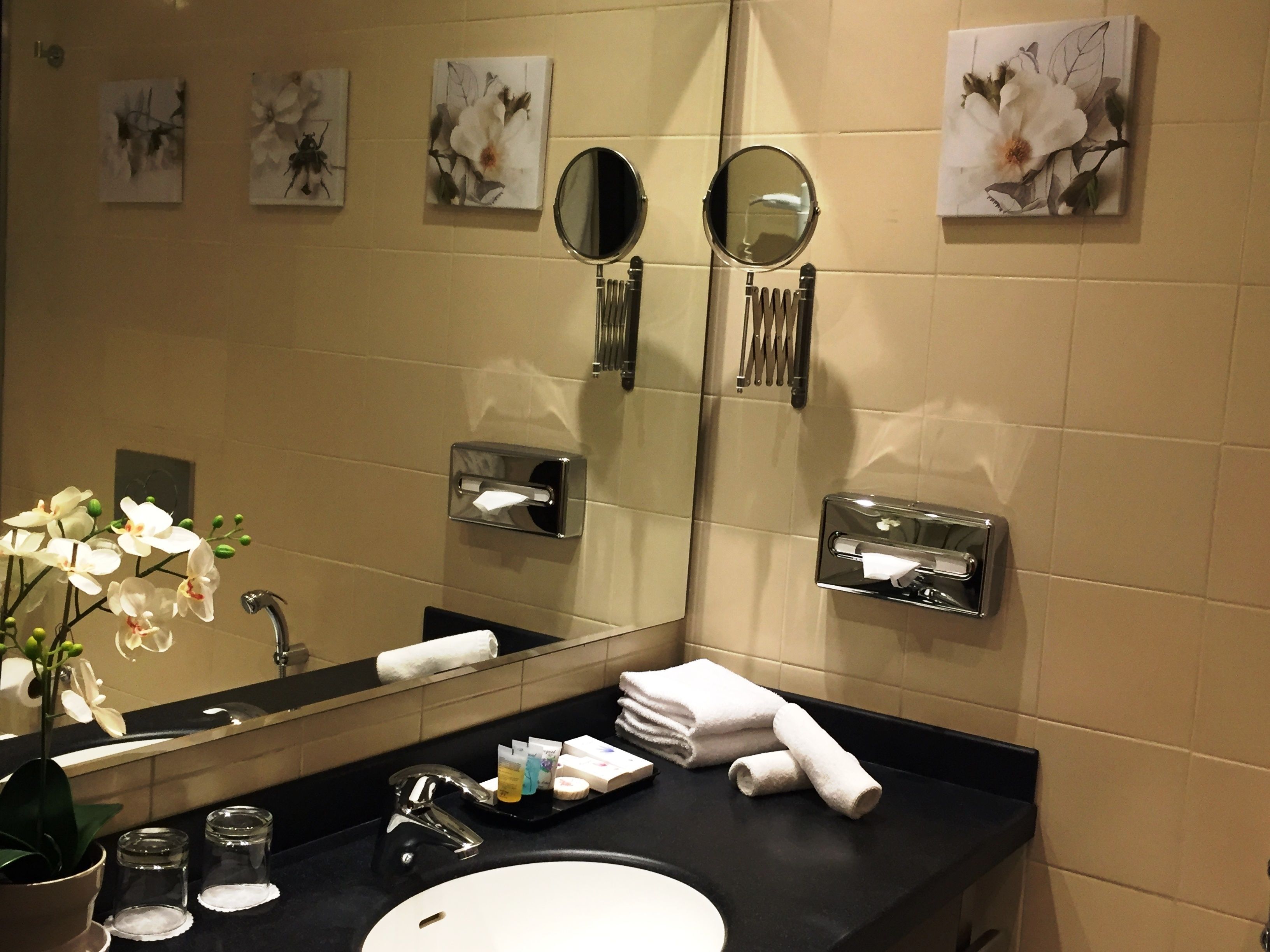 A bathroom with a large mirror, two wall-mounted mirrors, a sink, and a towel rack.