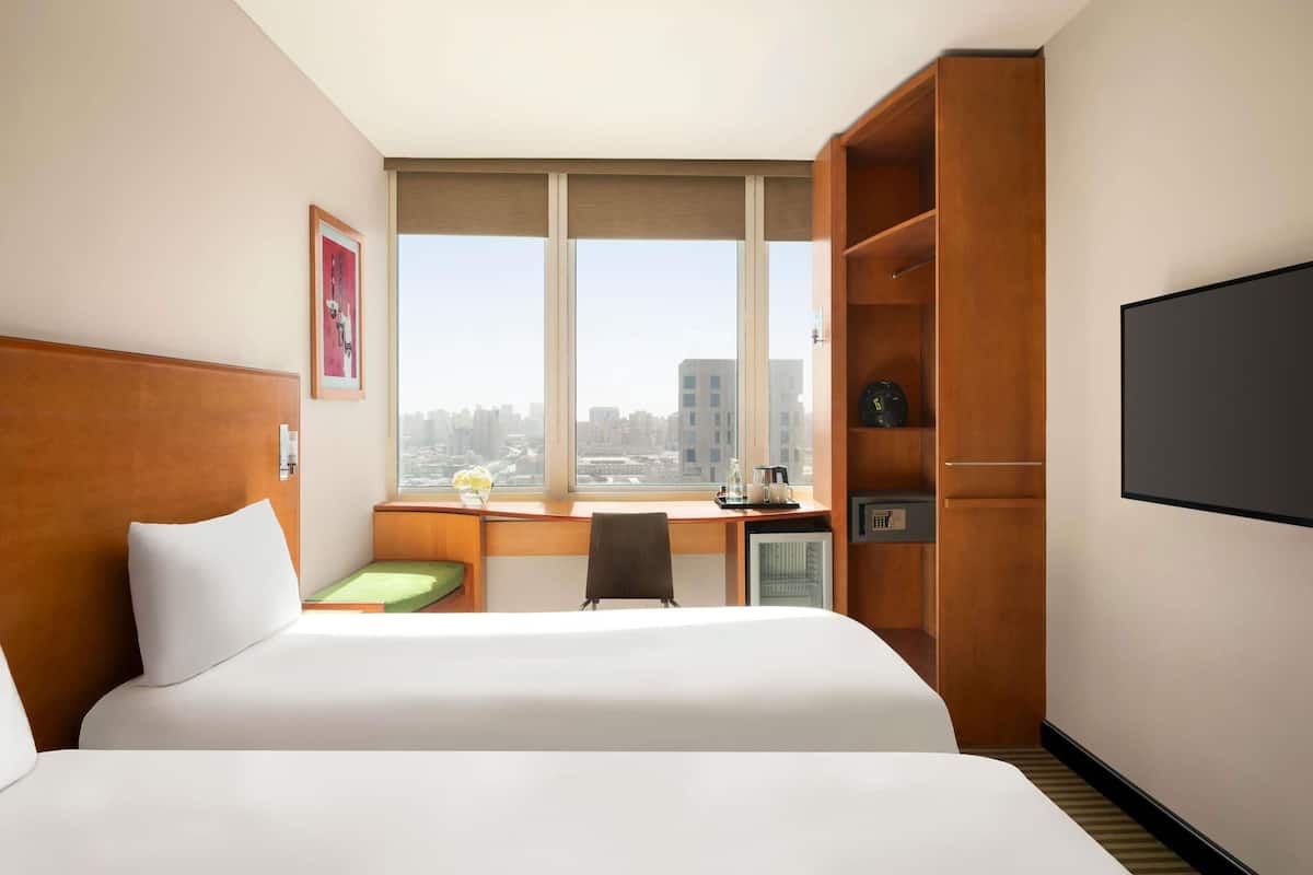A hotel room with a bed, a desk, a chair, a TV, and a view of the city.