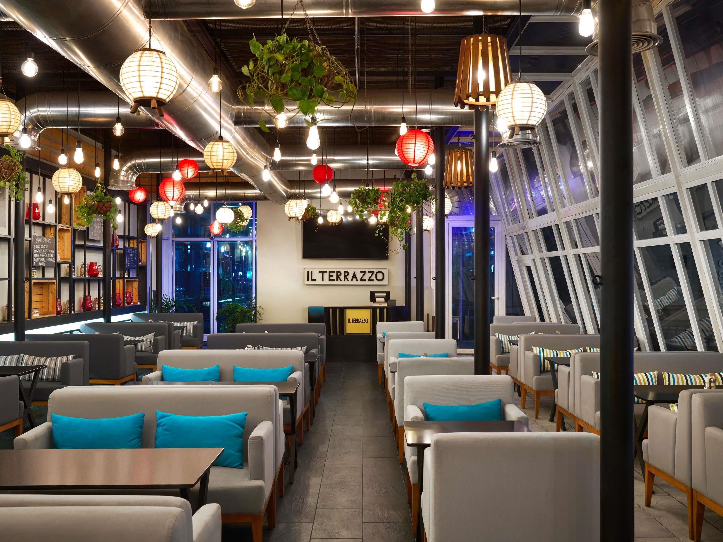 L’intérieur d’un restaurant, avec des tables, des luminaires suspendus et une enseigne indiquant « IL TERRAZZO ».